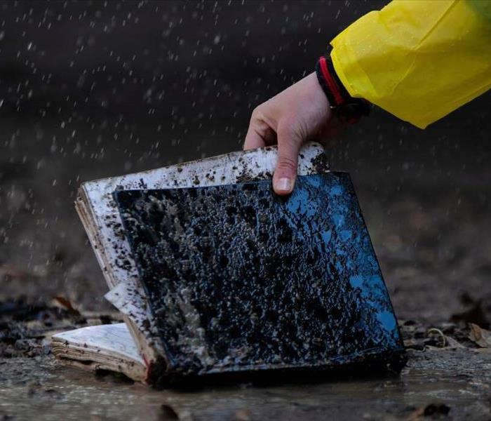 A hand reaching to pick up a book covered in mud and wet